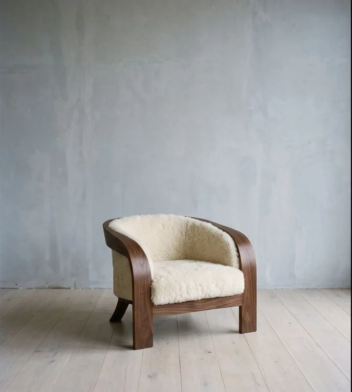 Cantilever lounge chair with a bent walnut frame and cream shearling cushions, photographed against a plain plaster wall.