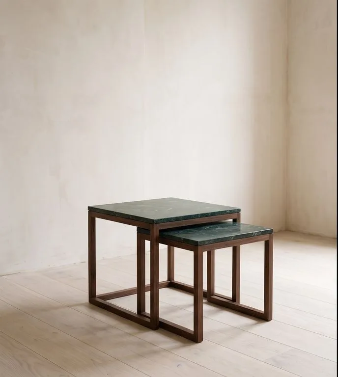 A pair of nesting tables with Verde Alpi tops on solid walnut slab sides, photographed against a plain plaster wall.